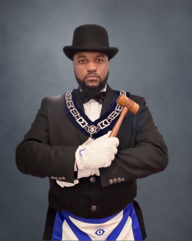 Worshipful Master Aaron Dixon-Saunders in top hat, collar, and apron, holding the gavel